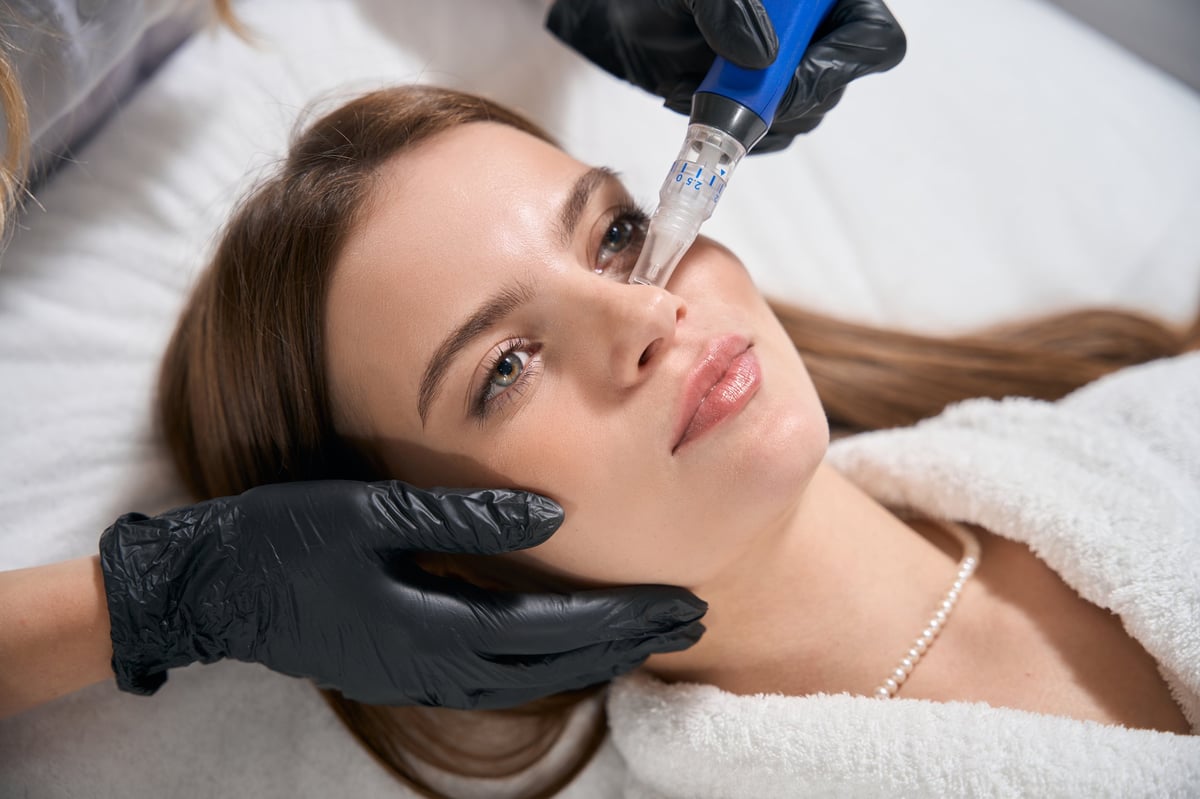 Partial female beautician doing ultrasonic cleaning of face skin with skinpen with micro needle of young caucasian woman in beauty salon